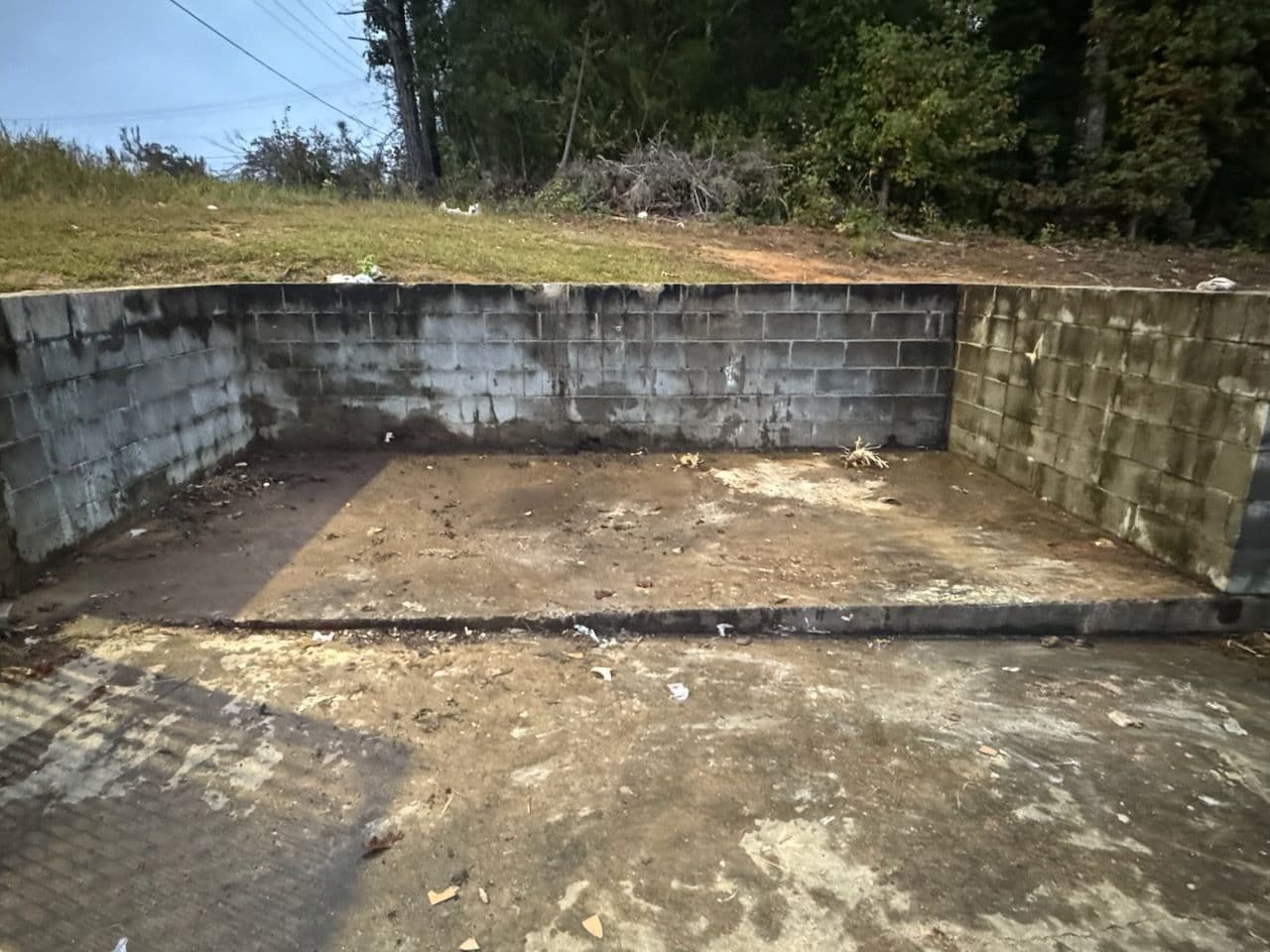 Abandoned concrete area with overgrown grass and trash along the perimeter.